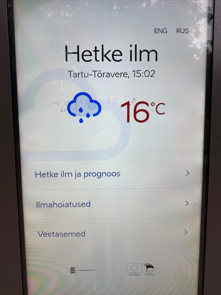 Baltikum 2025 – Lettland 2 – 7 Eine digitale Wetteranzeige zeigt „Hetke ilm“ mit Regensymbol, einer Temperatur von 16 °C und der Uhrzeit 15:02 Uhr in Tartu-Tõravere. Unter den Wetterinformationen sind Menüoptionen auf Estnisch aufgeführt.